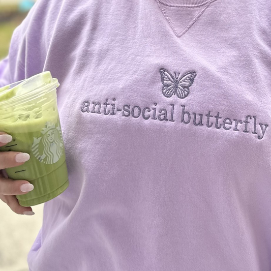girl wearing a lavender sweatshirt with a mini purple butterfly embroidered above the words anti-social butterfly on the chest