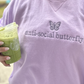 girl wearing a lavender sweatshirt with a mini purple butterfly embroidered above the words anti-social butterfly on the chest