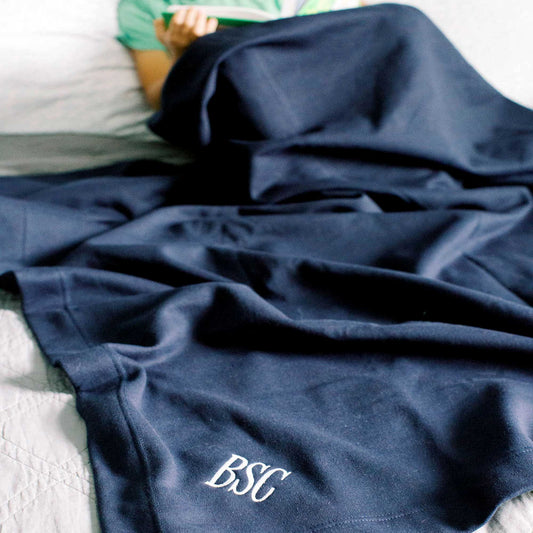 little boy reading on a bed with a large navy blue sweatshirt blanket featuring a corner monogram draped over his lap