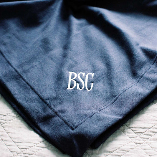 close up of personalized embroidered monogram on the corner of a dark blue cotton blanket