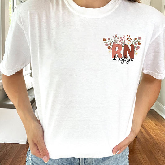 woman wearing a white t-shirt with a custom print on the left chest in a fall floral and color RN design with personalized script name