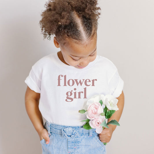 little girl holding flowers and wearing a white t-shirt with 'flower girl' printed in a mauve ink across the chest