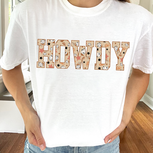 woman wearing a white comfort colors t-shirt with a HOWDY athletic print design with a cowboy ghost pattern fill