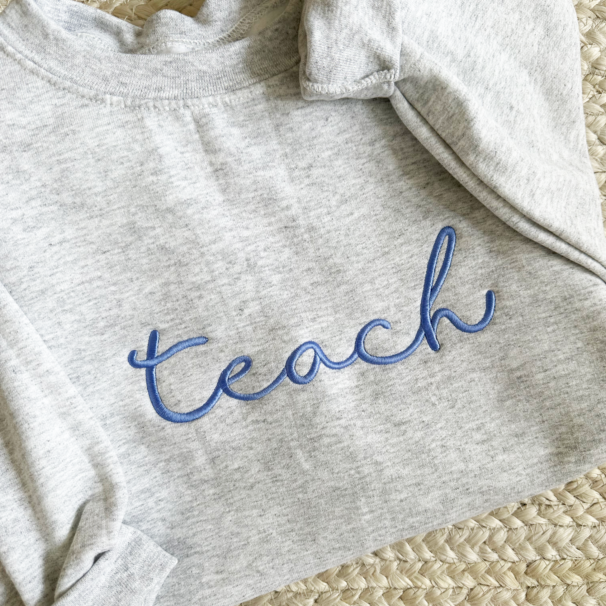 close up of embroidered teach script design on an ash crewneck sweatshirt