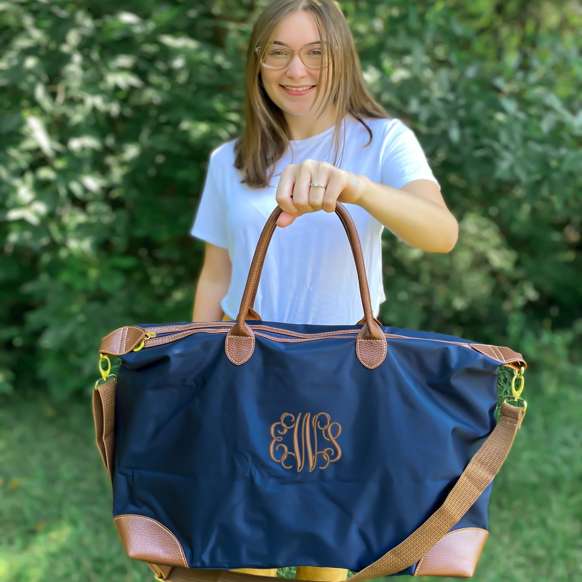 smiling woman with glasses holding navy nylon tote in front of her with one hand