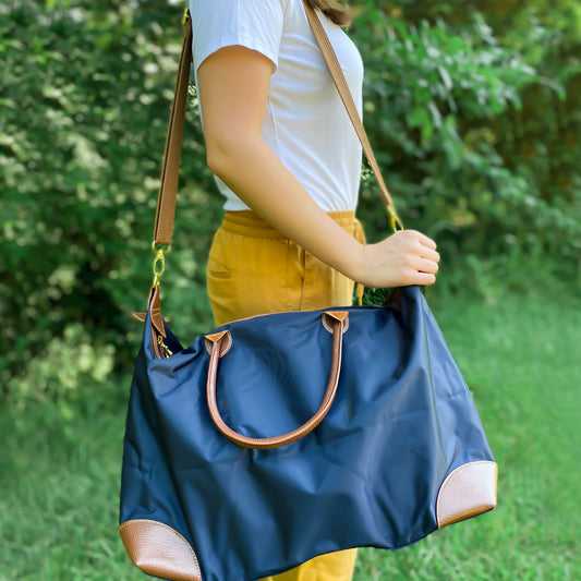 woman in white tee with mustard yellow pants holding navy nylon weekender on shoulder