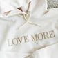 White hoodie showcasing LOVE More embroidered in all caps