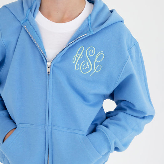 close up detail photo of a youth full zip jacket featuring a hood, metal full zipper, pockets, and a three letter monogram embroidered on a left chest
