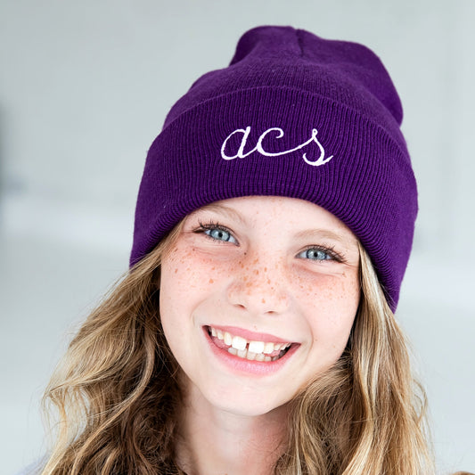 young girl wearing a purple beanie with a custom three letter monogram in a script lowercase font and lilac thread