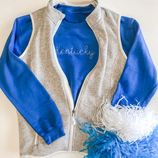 game day royal blue sweatshirt with a state name stitched across the chest in a white thread paired with a vest and pompoms