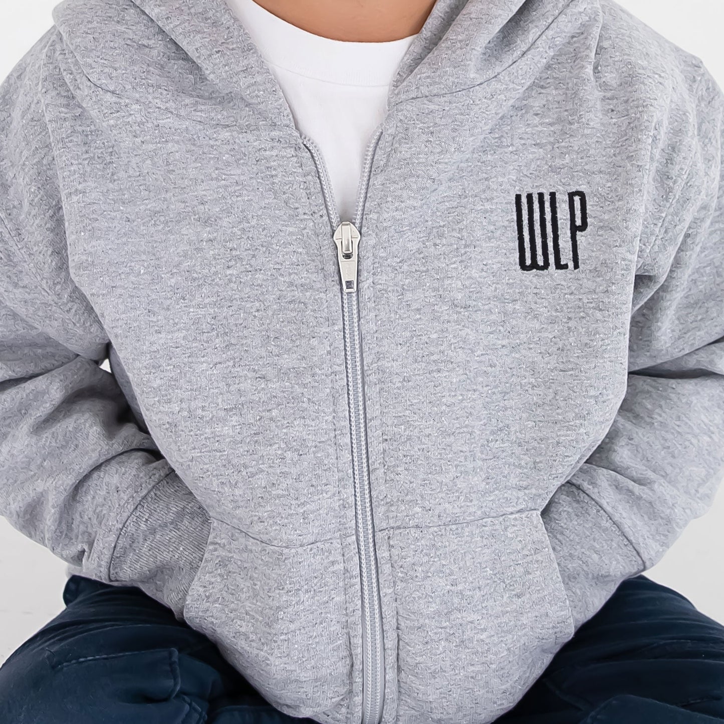 Detail photo of a toddler full zip jacket featuring a hood, silver full zip, pockets, and a personalized embroidered monogram in a navy thread on the left chest