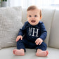 baby boy sitting on a couch wearing a long sleeved bodysuit in navy with a custom monogram in white thread on the chest.