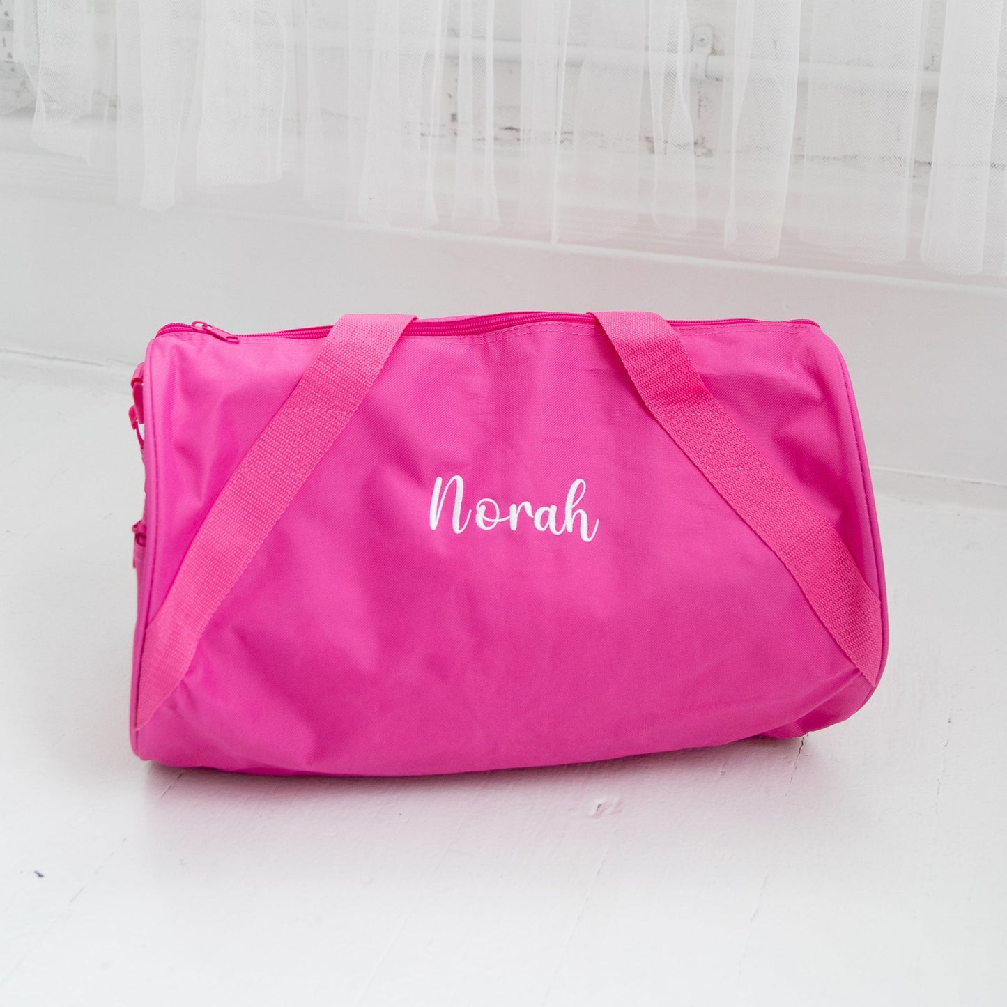 hot pink youth nylon duffle bag with crossbody strap featuring a name embroidery across the center 