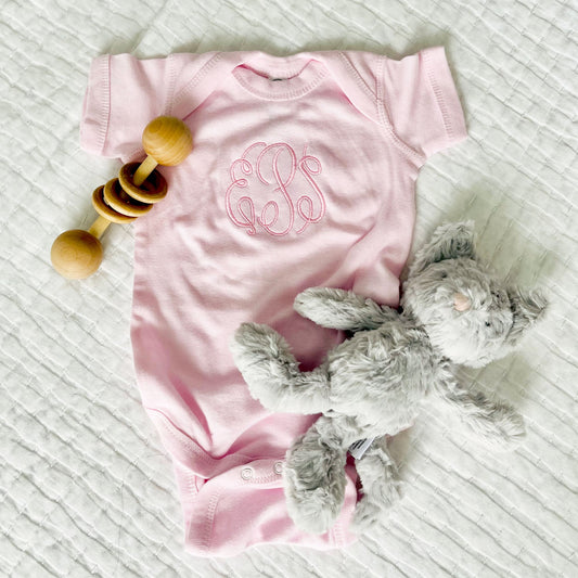flat lay image of a baby rattle, mouse stuffed animal, and baby pink short sleeve bodysuit with personalized large monogram on the center of the chest