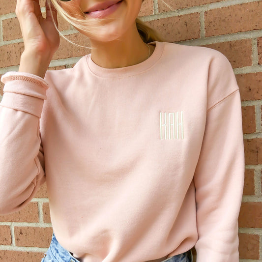 girl wearing a peach colored sweatshirt with custom three letter embroidered monogram on left chest 