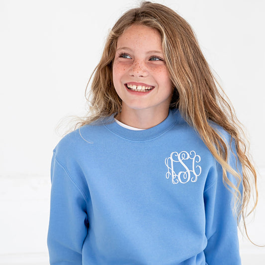 young girl smiling and wearing a carolina blue crewneck sweatshirt with a personalized three letter monogram embroidered in a script font on the left chest