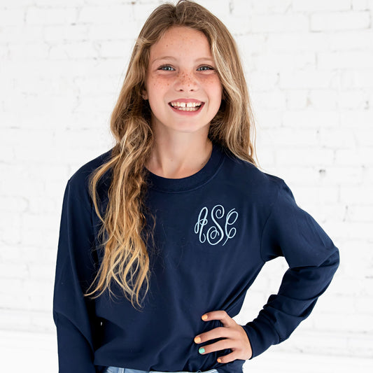 girl smiling and wearing a navy blue long sleeved top with a script three letter monogram embroidered on the left chest in a light blue thread
