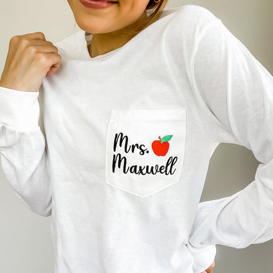 girl wearing long sleeved pocket t-shirt with teacher name and small red apple embroidered on the pocket 