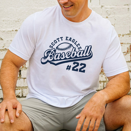 man wearing a white t-shirt with a custom design printed in blue ink featuring a basebal team name, a baseball, the word baseball in a varsity script font, and a player's number