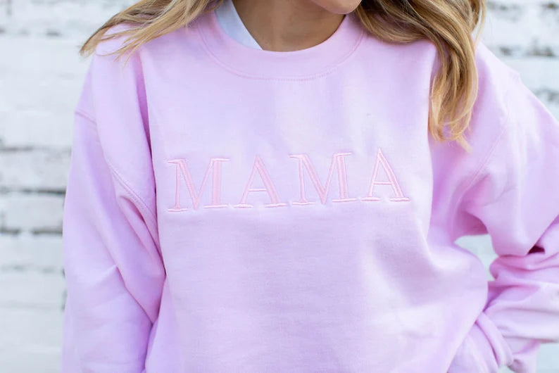 close up of a light pink crewneck sweatshirt with embroidered mama in baby pink thread an in all caps across the chest