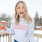 girl throwing snow outside holding a coffee cup and wearing an ash gray crewneck sweatshirt with a festive MERRY design in a pastel pink mini santa design
