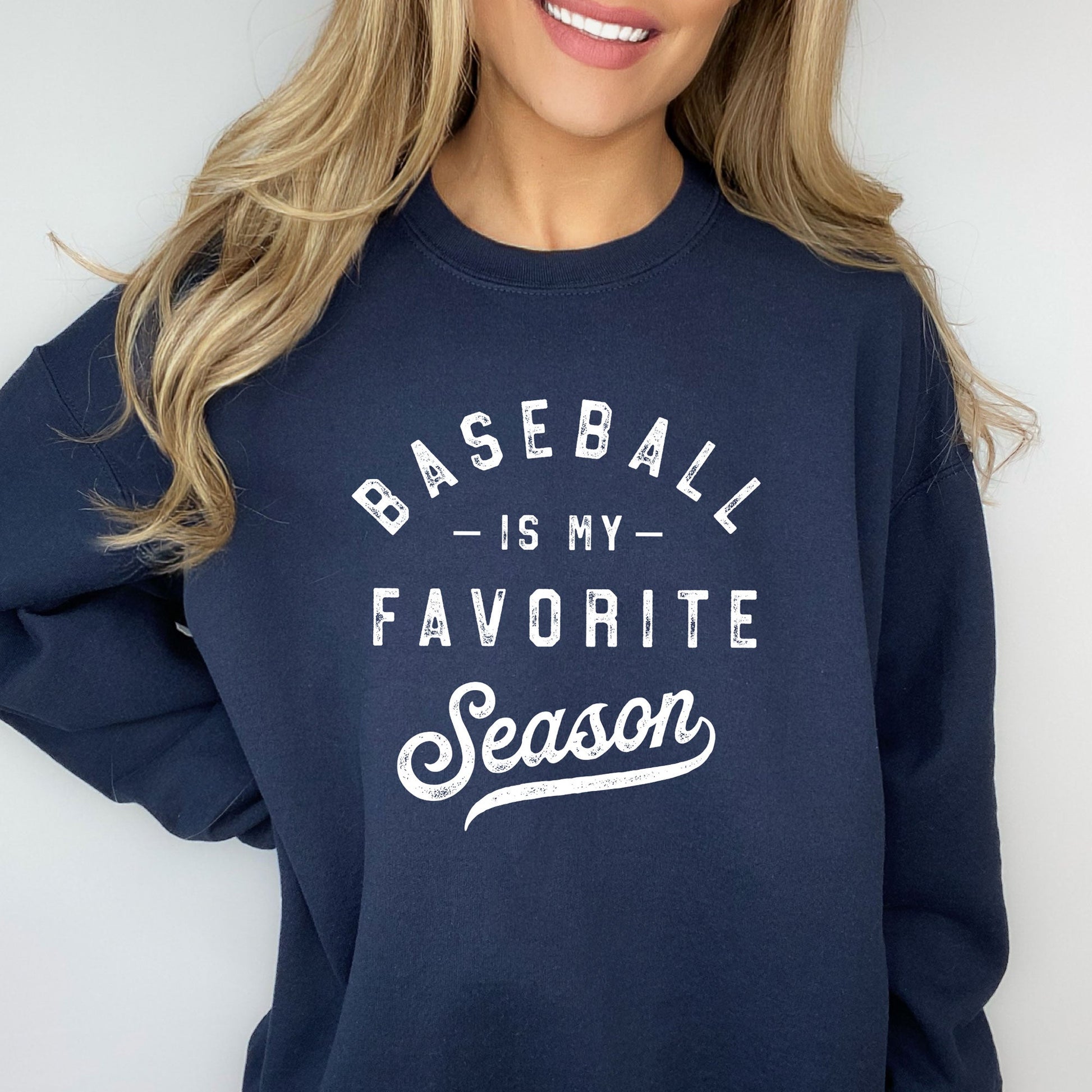 woman wearing a navy sweatshirt with a distressed white ink print reading "baseball is my favorite season"