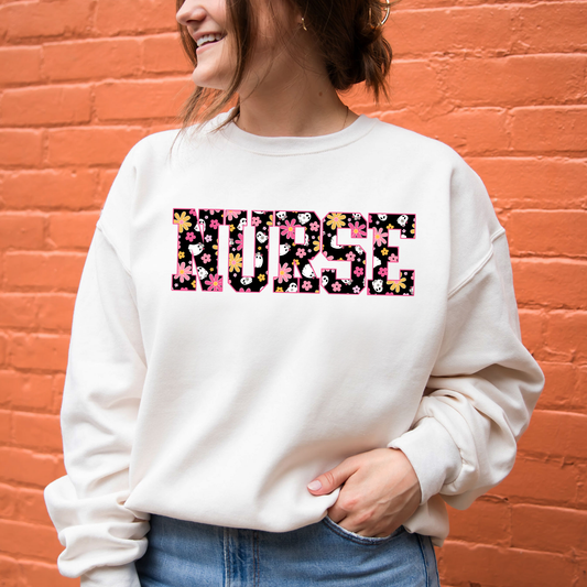 woman wearing a crewneck sweatshirt featuring a NURSE groovy daisy ghost pattern