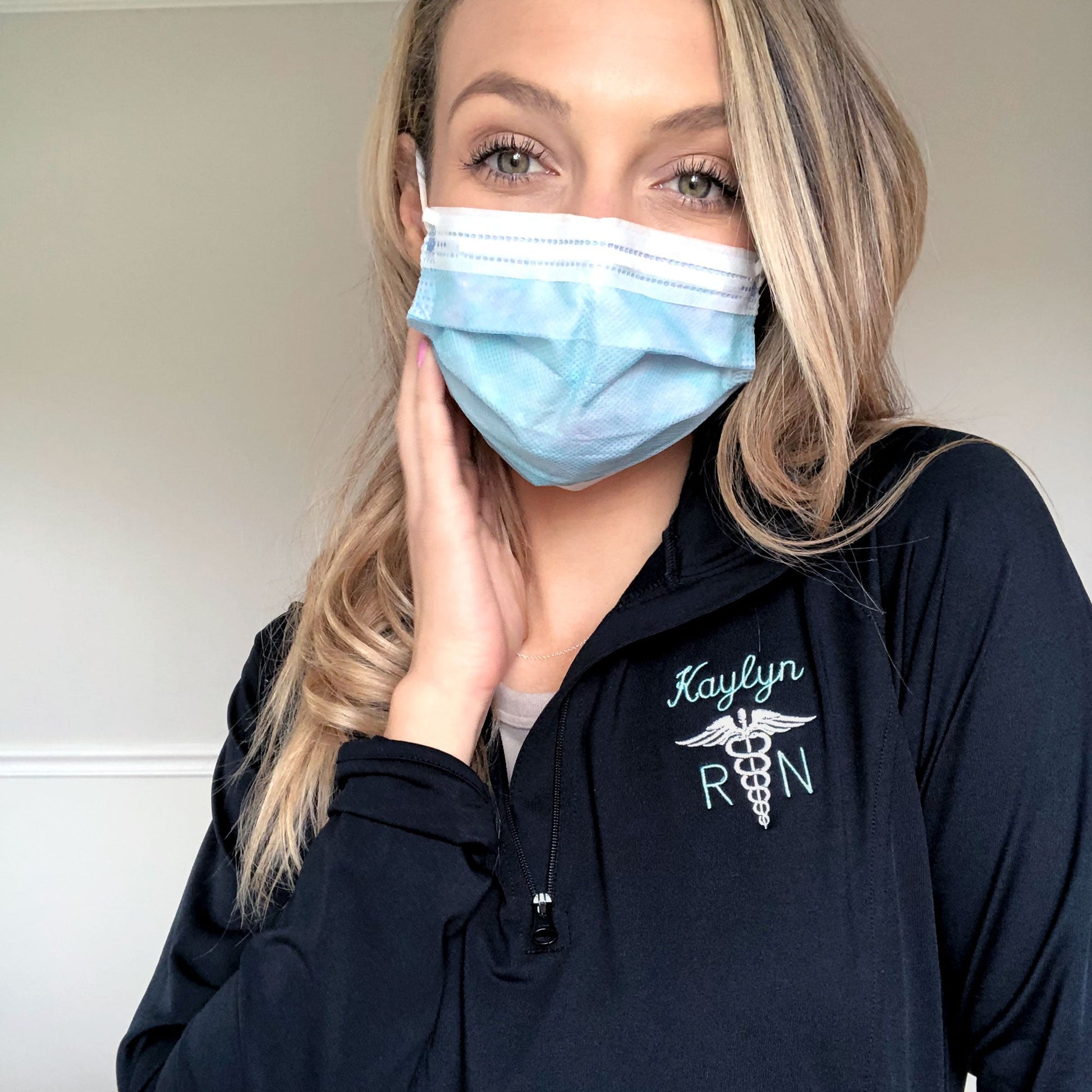 woman posing wearing medical mask wearing sporty quarter zip with name and credentials embroidered with caduceus