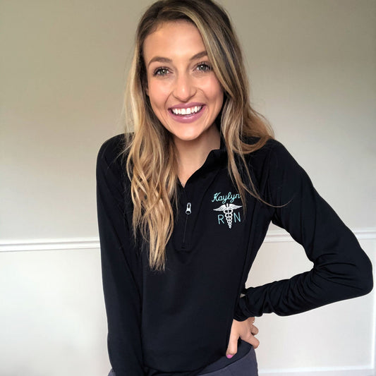 woman smiling wearing black athletic quarter zip jacket with caduceus embroidery on left chest