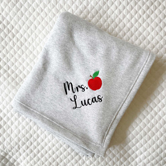 grey folded stadium blanket with a personalized name and apple embroidered design