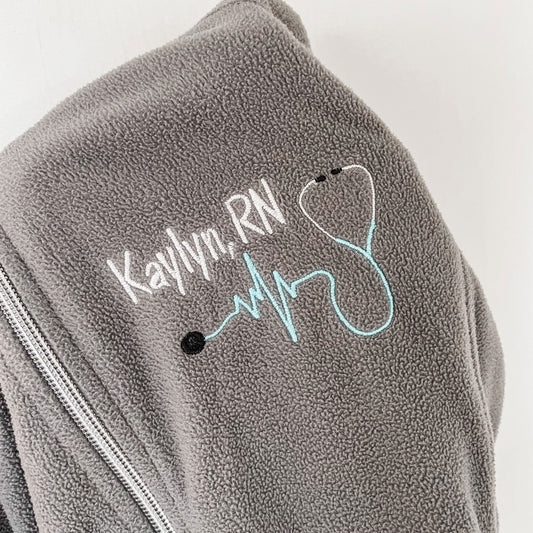 close up of a custom nurse embroidery design on a lightweight fleece full zip jacket featuring name, credentials, and a heartbeat stethoscope