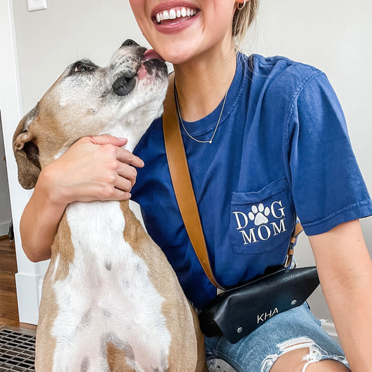 young woman posing with her dog while wearing a navy blue short sleeved pocket tee with dog mom embroidered on the pocket.