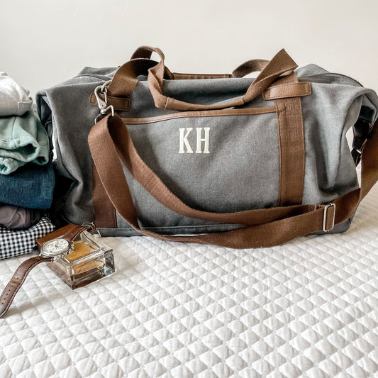 photo of gray duffel with clothing, watch and cologne beside it 