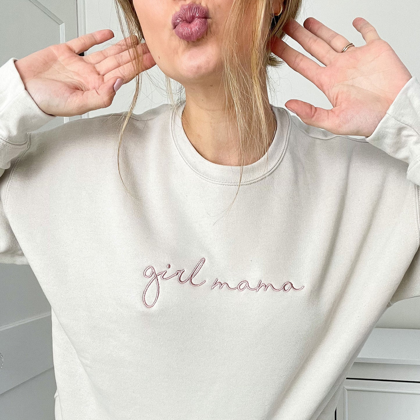 woman wearing a beige crewneck bella and canvas crewneck with girl mama embroidered across the chest in a mauve thread 