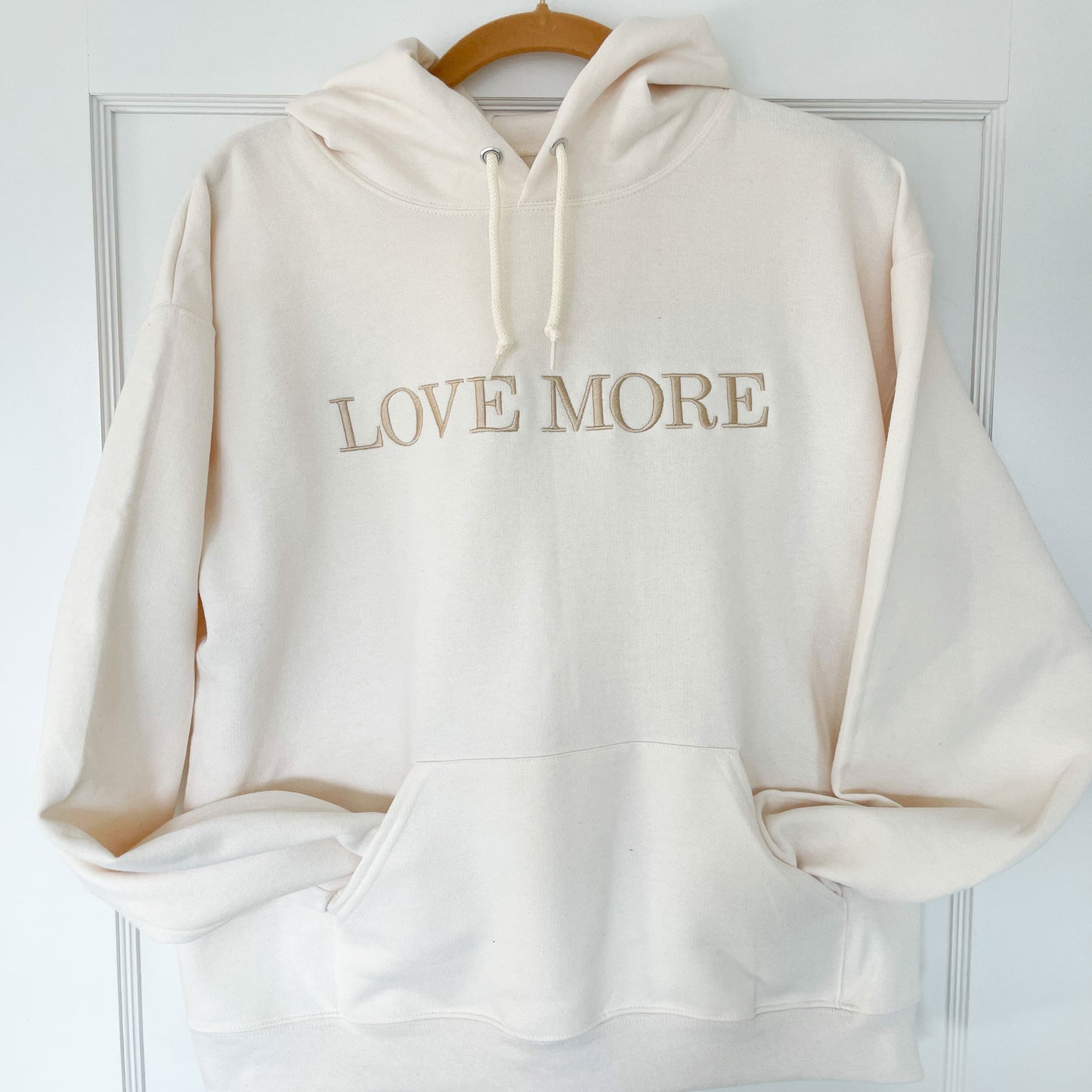 White hoodie with embroidered LOVE MORE in capital text across the chest 