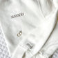 White crewneck sweatshirt with a roman numeral date embroidered on the left chest and cuff embroidery on the sleeve