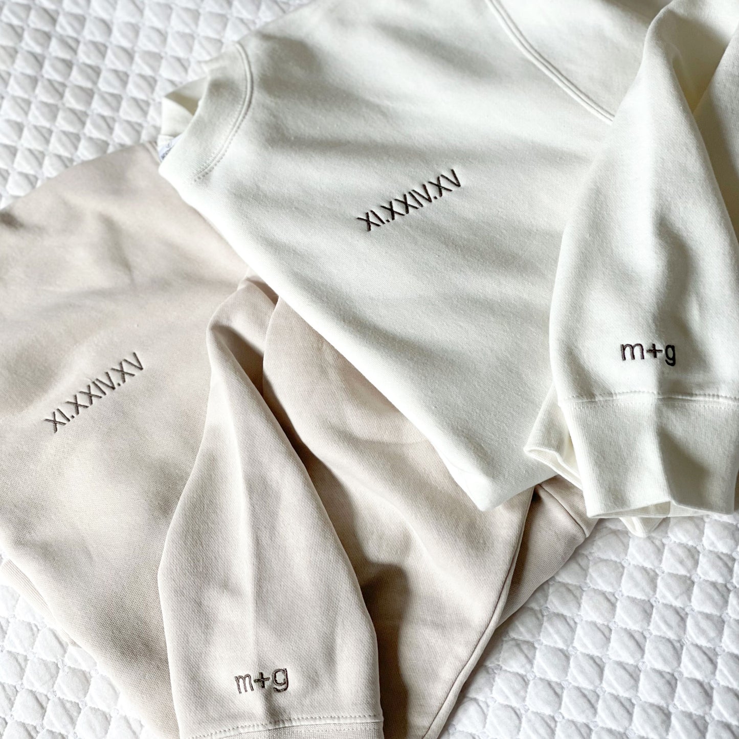 two crewneck sweatshirts showcasing an embroidered roman numeral date embroidered on the left chest and matching initials on the cudd