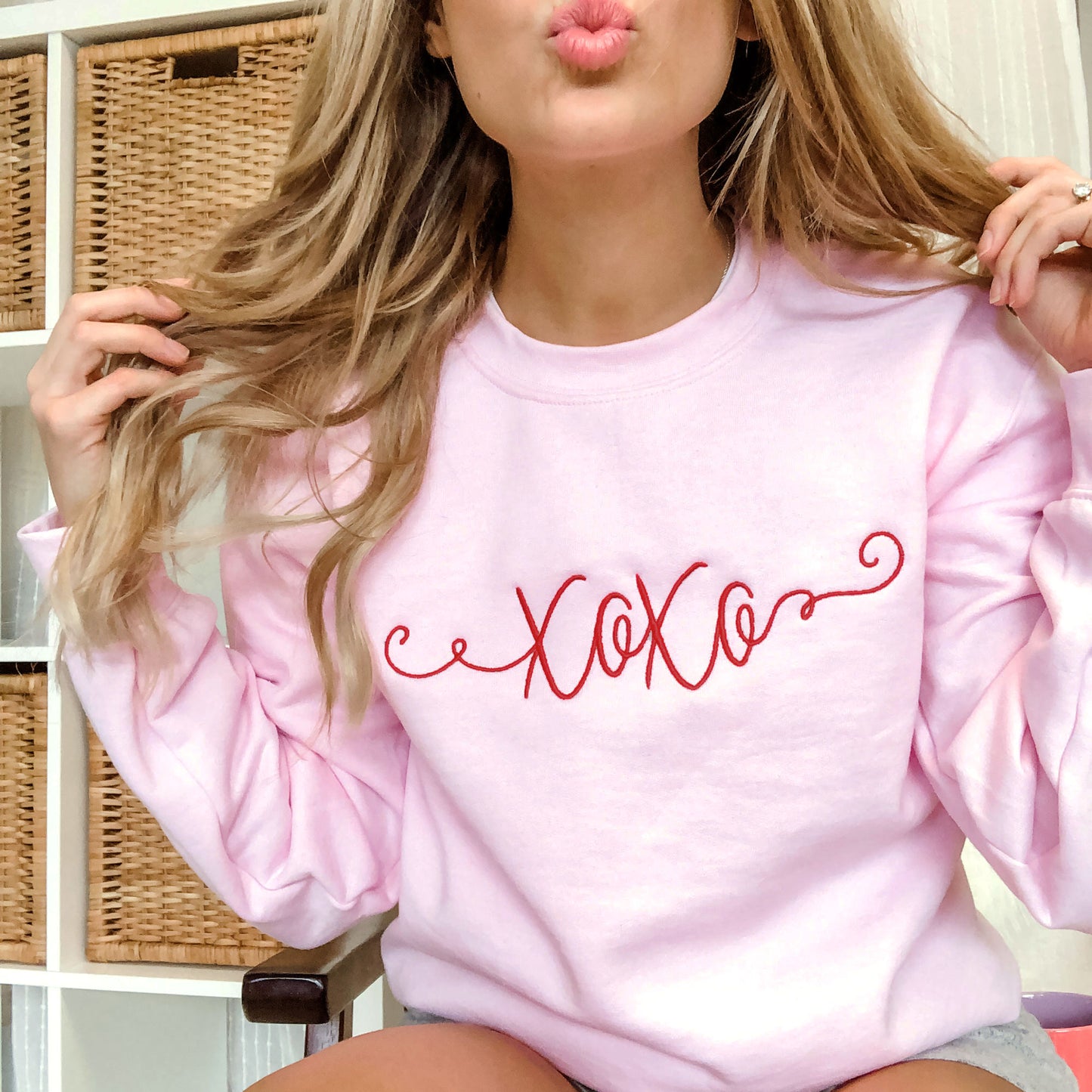 girl wearing a pink pullover crewneck sweatshirt with xo xo embroidered in a curly script font in a dark red across the chest 