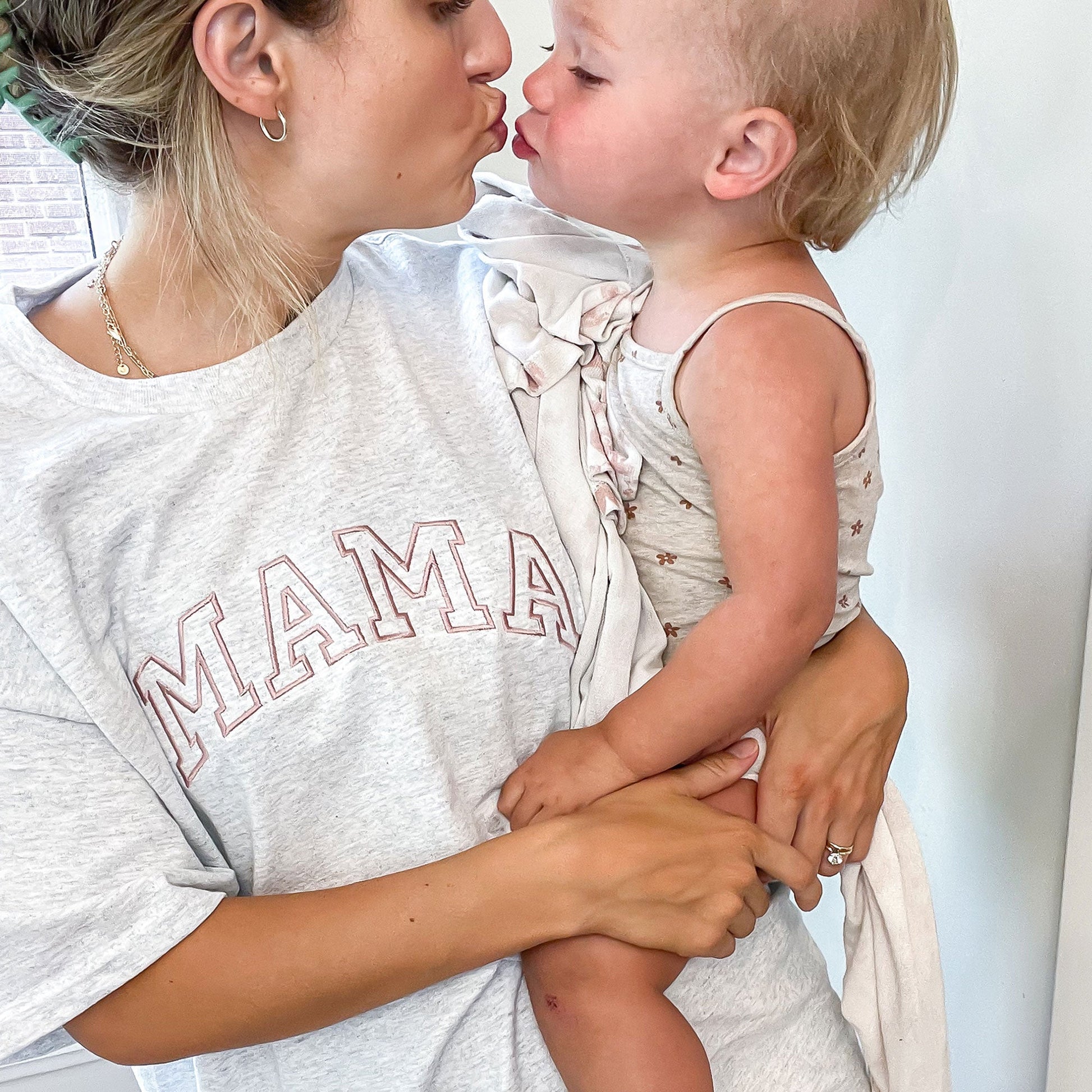 a woman wearing a light gray mama t-shirt with custom mama embroidery in mauve thread holding her child