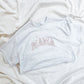 flat lay of gray t-shirt with mama embroidered across the chest in pink thread and in an athletic block font