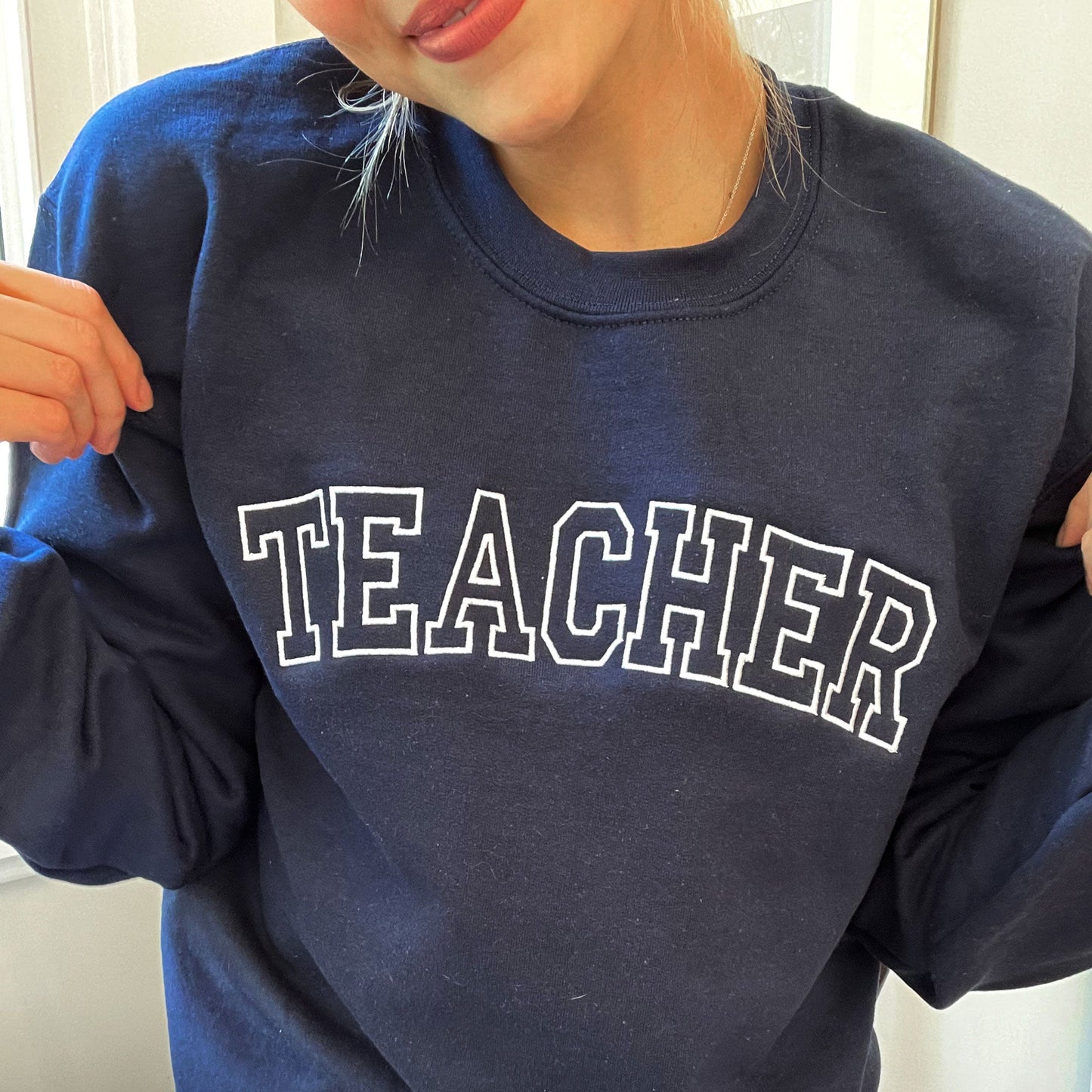 an educator wearing a casual pullover sweatshirt in navy with custom embroidery reading teacher in a vintage font