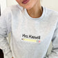 close up of girl wearing an ash crewneck sweatshirt with custom name and pencil embroidery on the middle of the chest 