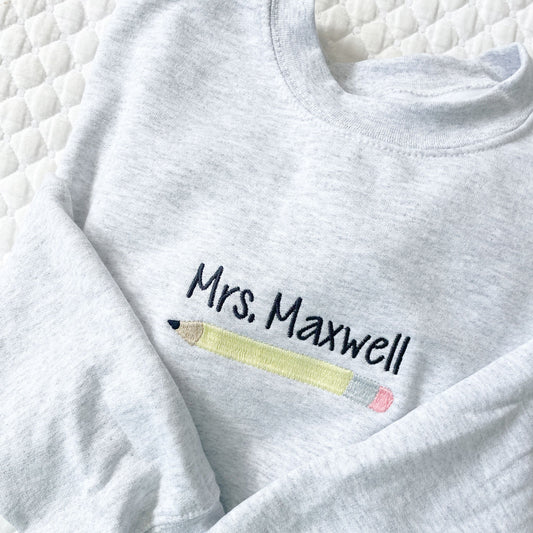close up of custom embroidery featuring an educators name and a yellow number two pencil on a sweatshirt