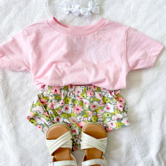 cute toddler outfit layout featuring a light pink tee with a white monogram design on the left chest