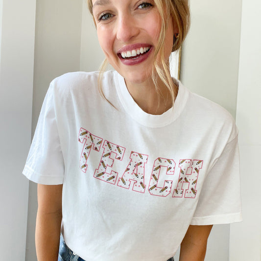 woman wearing a white t-shirt with TEACH printed in a mini pencil and star pattern across the chest