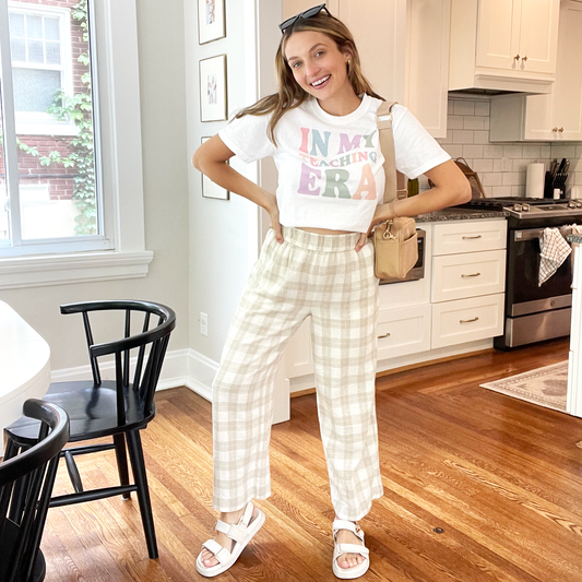 girl wearing a styled outfit. plaid pants, sandles, crossbody bag, and a white comfort colors t-shirt with a 'in my teaching era' print