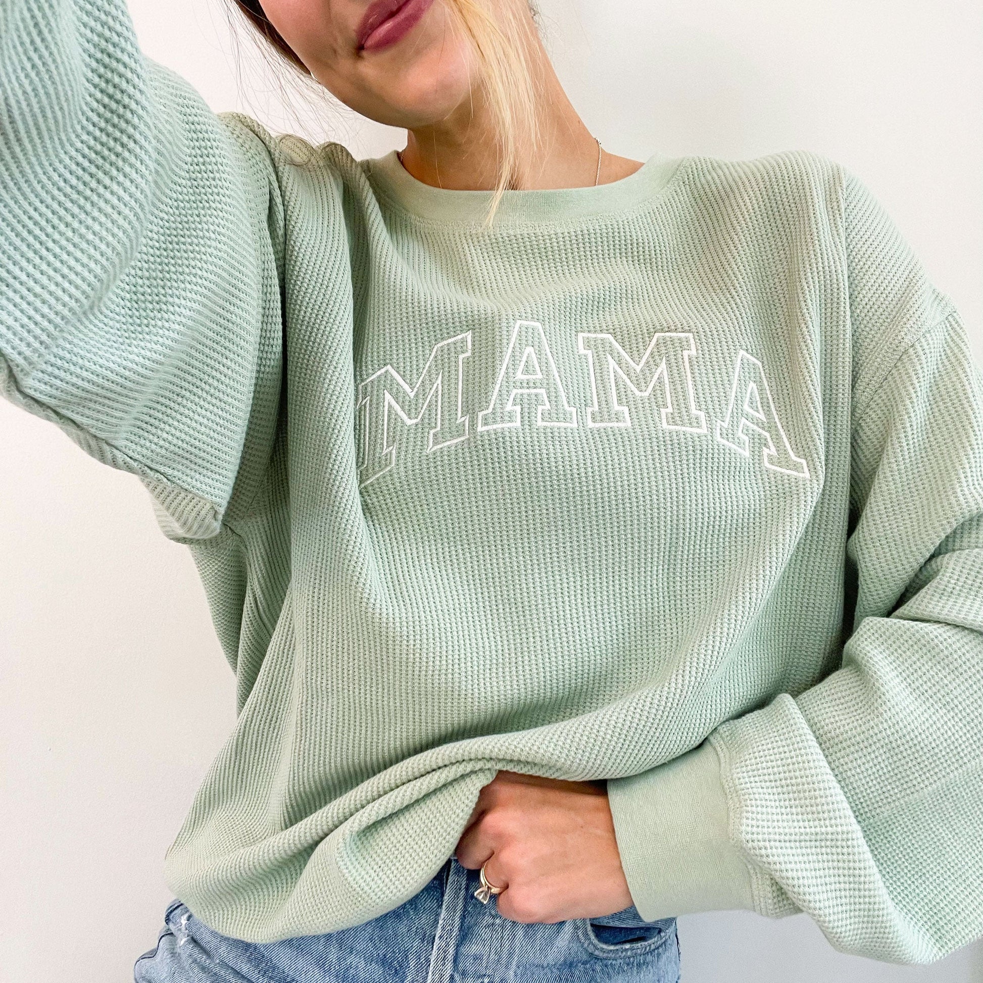 woman wearing oversized sage green waffle knit crewneck sweatshirt with mama embroidered in large block letters across the chest