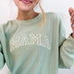 a mom wearing an oversized waffle knit pullover crewneck with mama embroidered in an outlined athletic block font across the chest