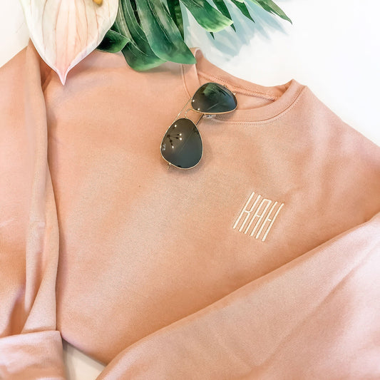flat lay of peach crewneck sweatshirt with embroidered three letter monogram in natural thread.