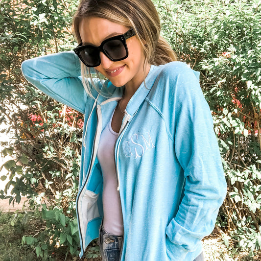 woman wearing sunglasses and a lightweight french terry jacket with a hood and personalized monogram embroidery on the left chest
